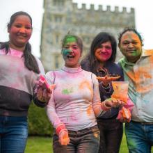 Four students celebrating Holi, covered in paint dust and smiles in front of Hatley Castle.