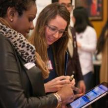 Two people looking at an iPad in a crowded conference room.