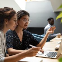 Two people sitting in front of a laptop looking thoughtfully at an assignment.
