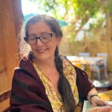 Smiling women sitting at a table with a long braid and glasses.