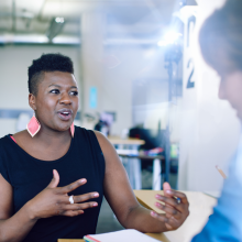 A young black woman gestures to a classmate as though describing something she is passionate about. A spark of light behind her speaks to a bright future ahead.