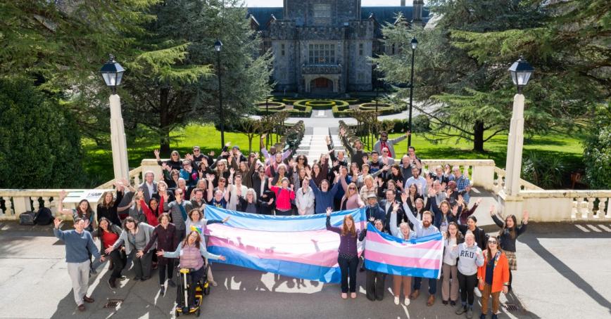 Dozens of people hold a giant trans flag outside of Hatley Castle in honour of Trans Day of Visibility.
