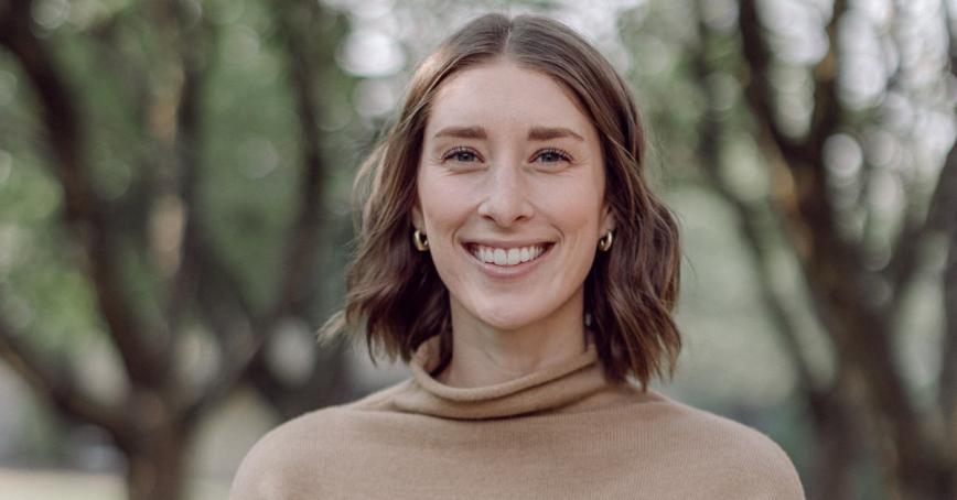 close up of woman smiling at the camera. She has short brown hair and is wearing a tan coloured shirt.